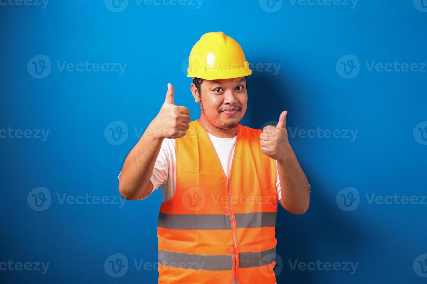 trabalhador da construção civil asiático gordo vestindo colete de segurança laranja e capacete mostrando sinal de polegar para cima foto