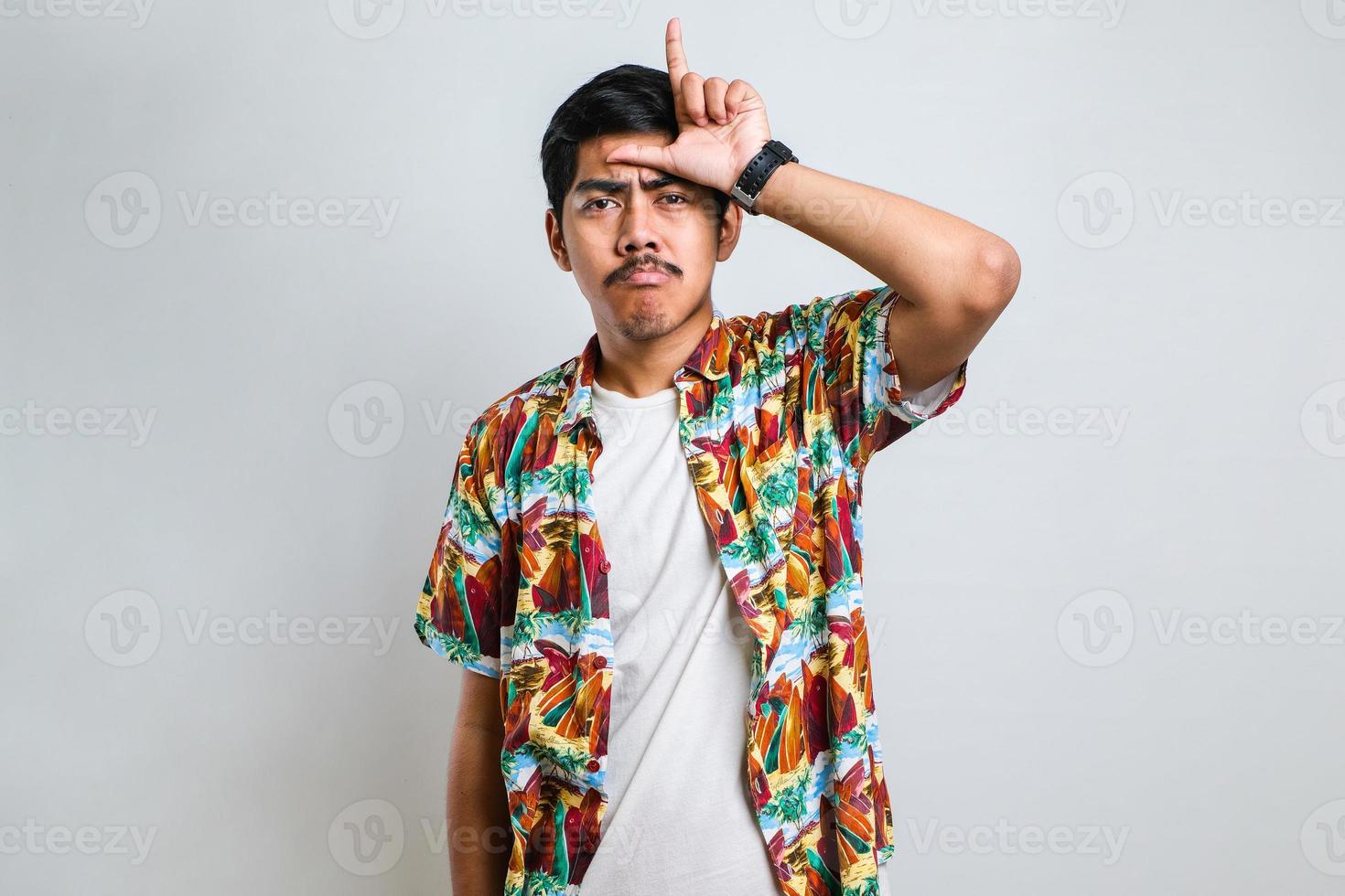 homem vestindo camisa casual tirando sarro de pessoas com dedos na testa fazendo gesto de perdedor foto