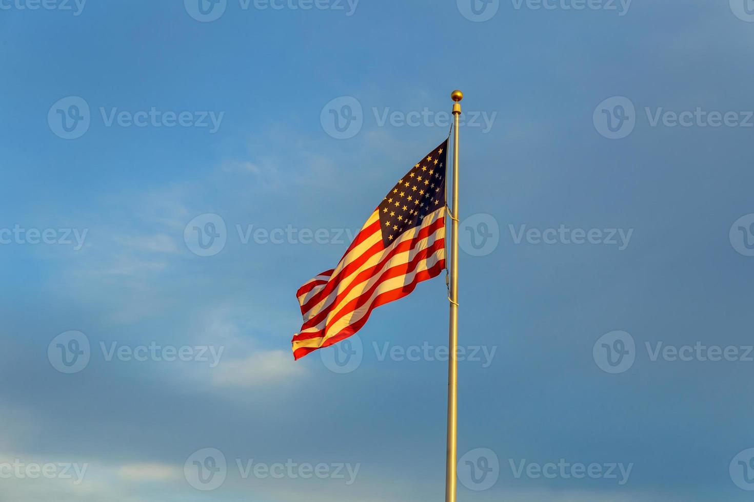 bandeira americana no mastro da bandeira balançando ao vento contra nuvens, céu azul foto