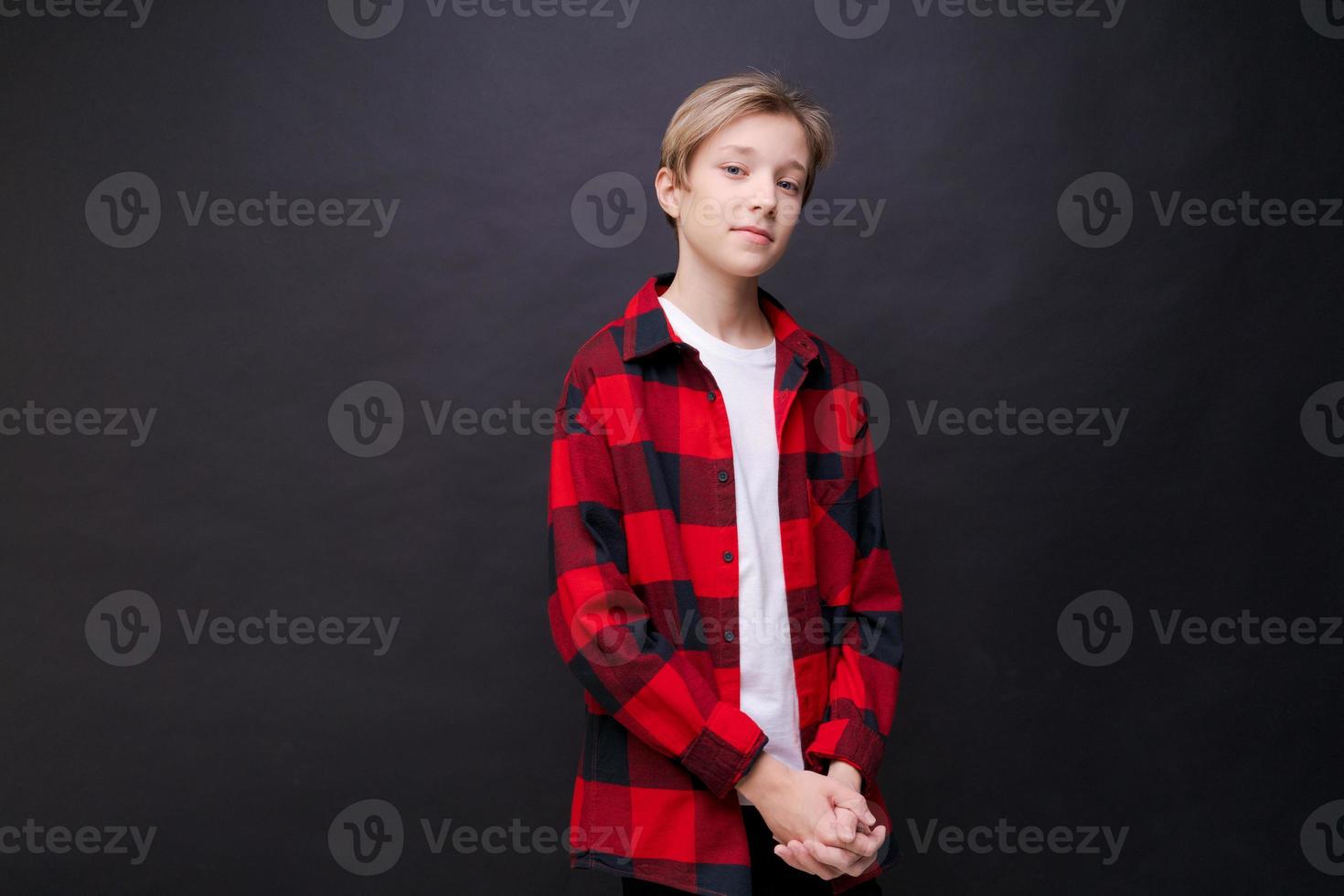 menino bonitinho na camiseta branca e camisa vermelha na gaiola posando em preto foto