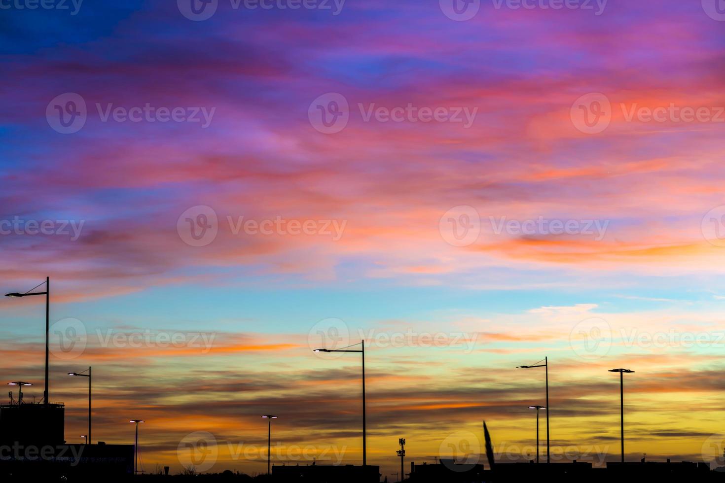 céu ao pôr do sol com nuvens sombreadas nas cores vermelho laranja amarelo e azul e com lâmpadas de rua retroiluminadas foto