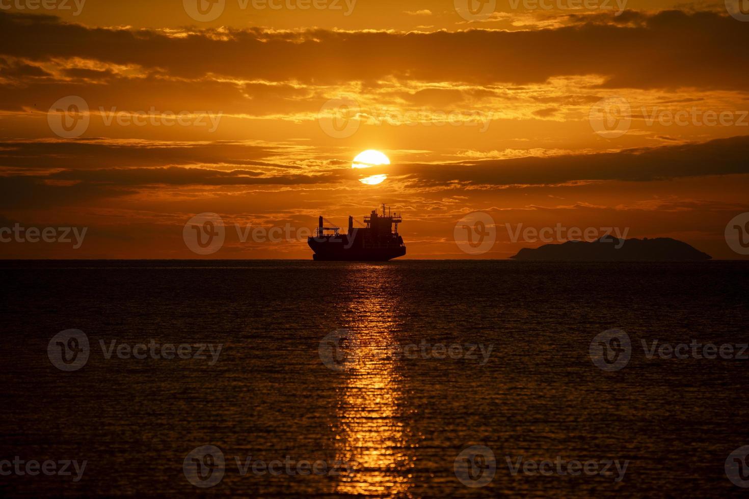 navio de carga ao pôr do sol em contraluz com ilha ao fundo foto