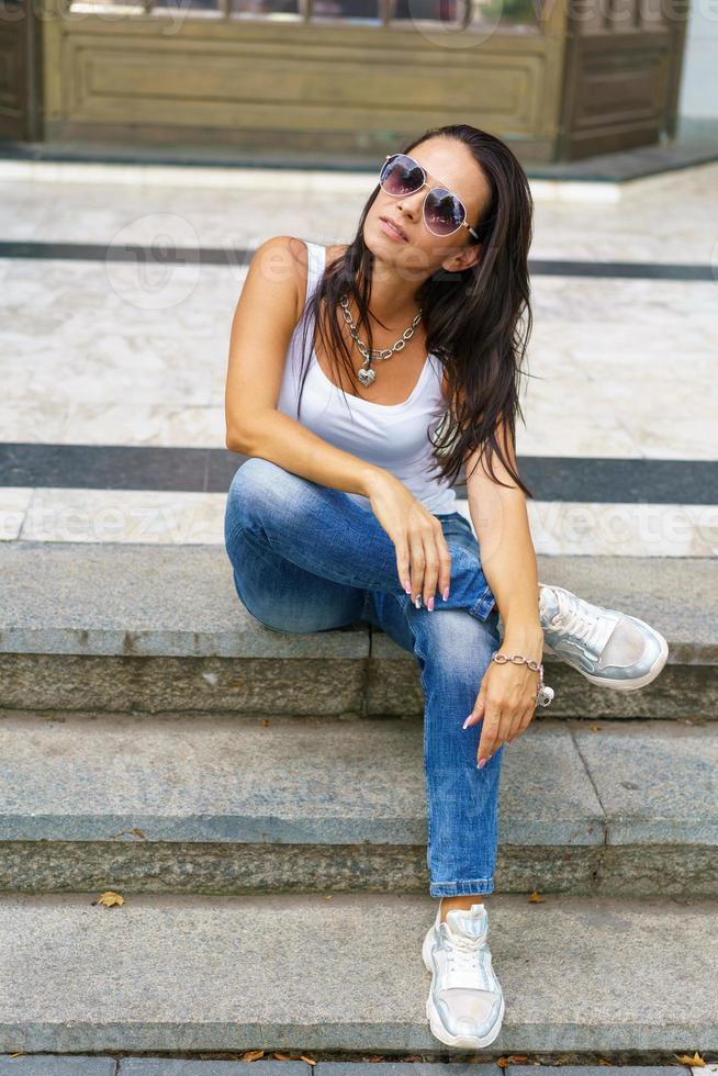 estilo casual. mulher elegante em óculos de sol, sentado em uma escada de pedra. ela era foto