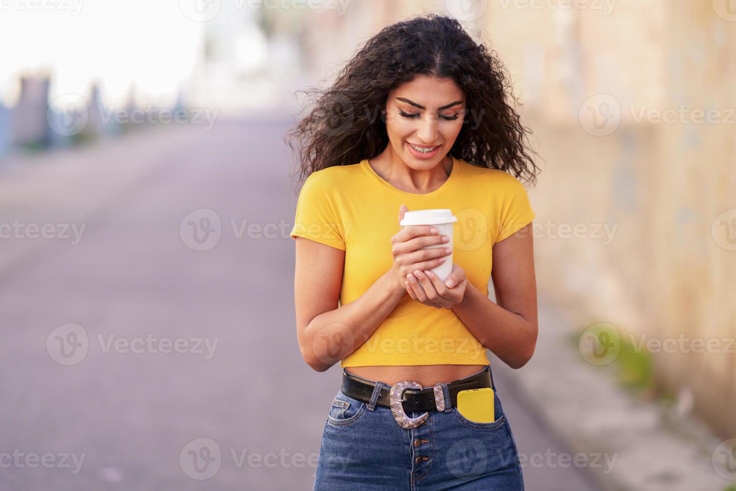 menina árabe atravessando a rua com um café para viagem foto