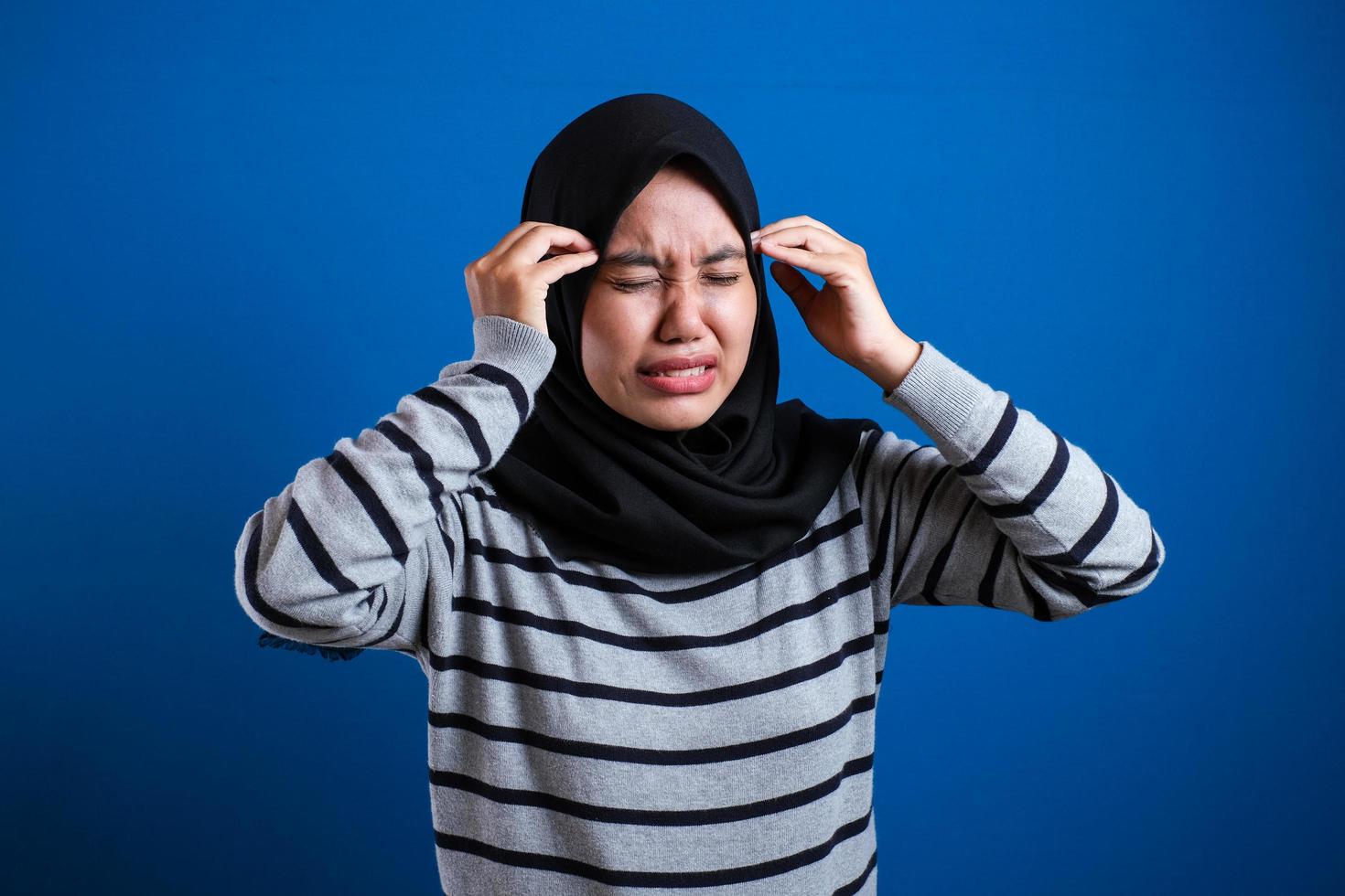 adolescente muçulmana asiática segurando a cabeça e fechando os olhos foto
