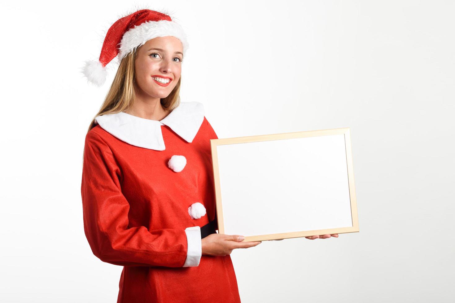 mulher loira sorridente com roupas de papai noel com quadro branco foto