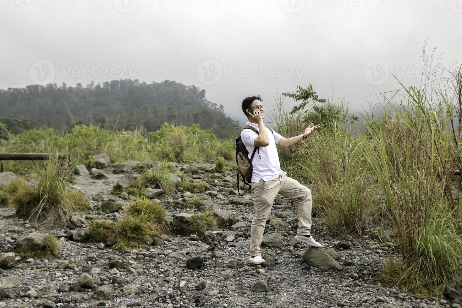 homem jovem mochileiro asiático está feliz e sorri quando ele olha smartphone em viagem de montanha foto