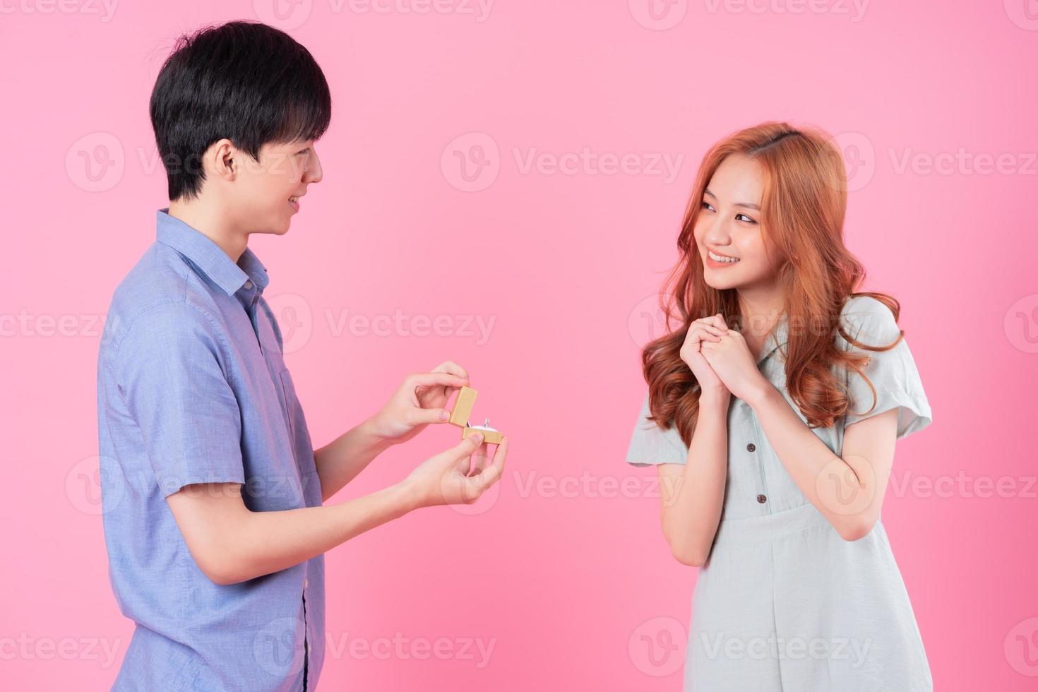 jovem asiático propõe a namorada em um fundo rosa foto