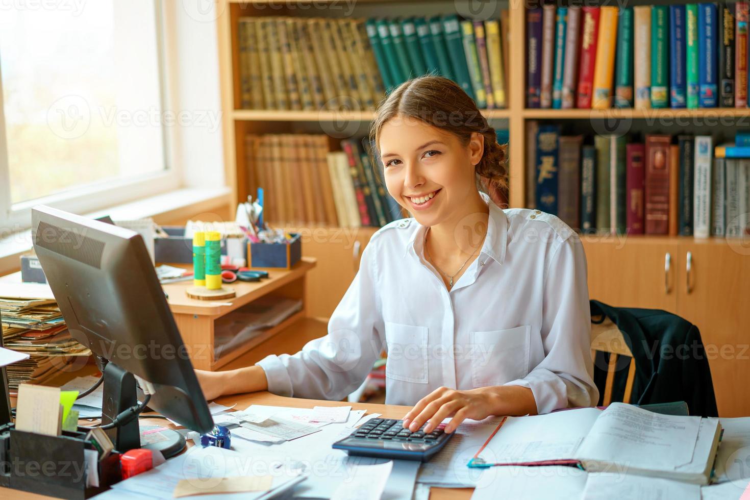 jovem senhora de negócios feliz na camisa branca, sentado à mesa com computador e papel ambiente de trabalho foto