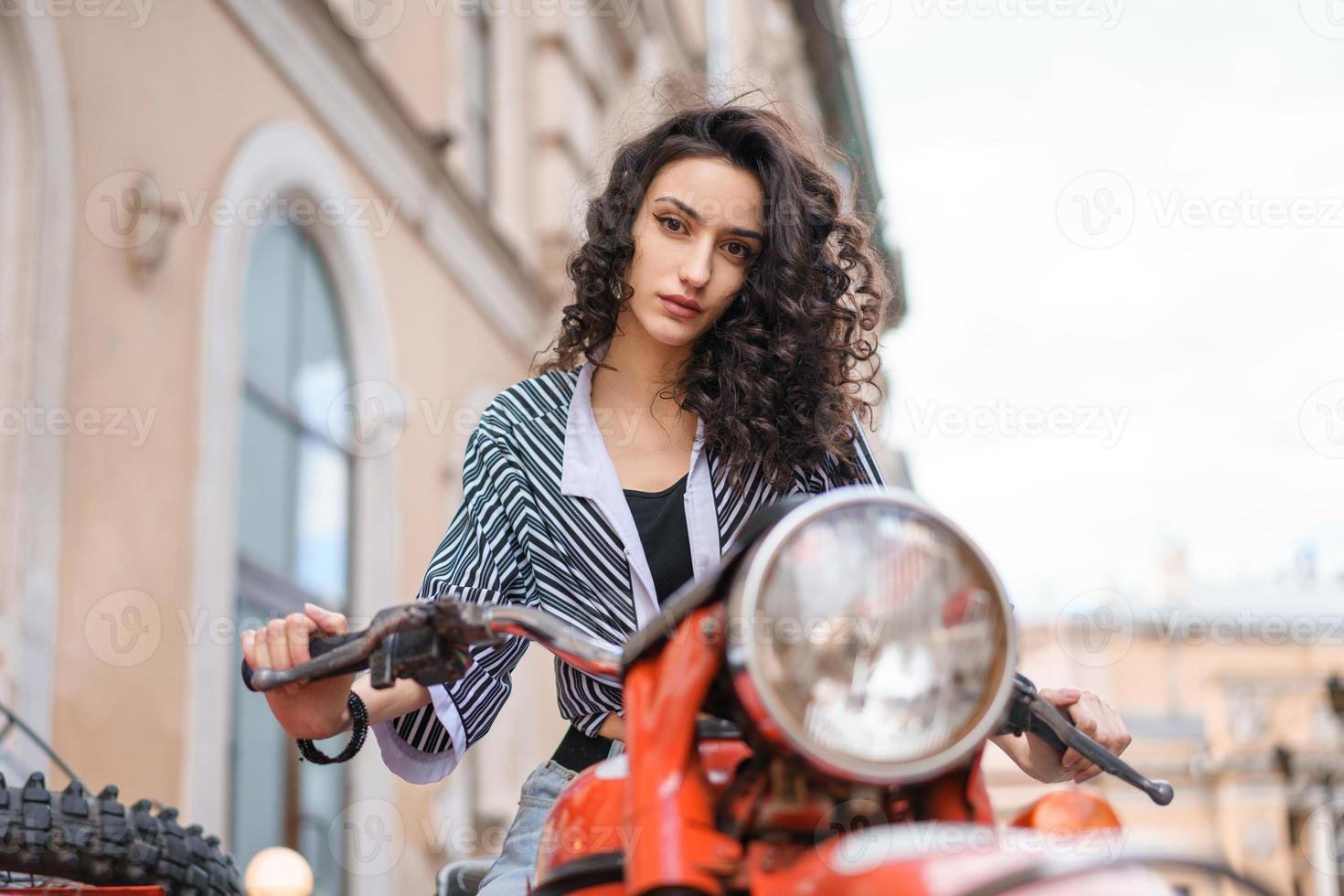 bela jovem sentada em uma motocicleta em uma rua da cidade foto