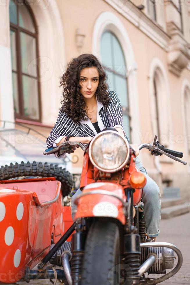 a garota senta-se em uma motocicleta no contexto da cidade. foto