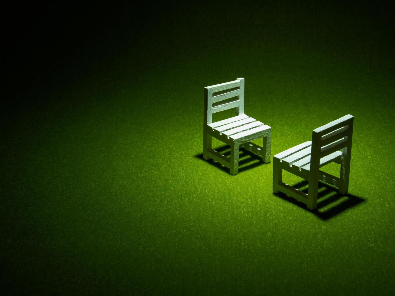 cadeiras de madeira brancas na grama artificial. luz brilhando de cima no tom escuro baixa chave foto