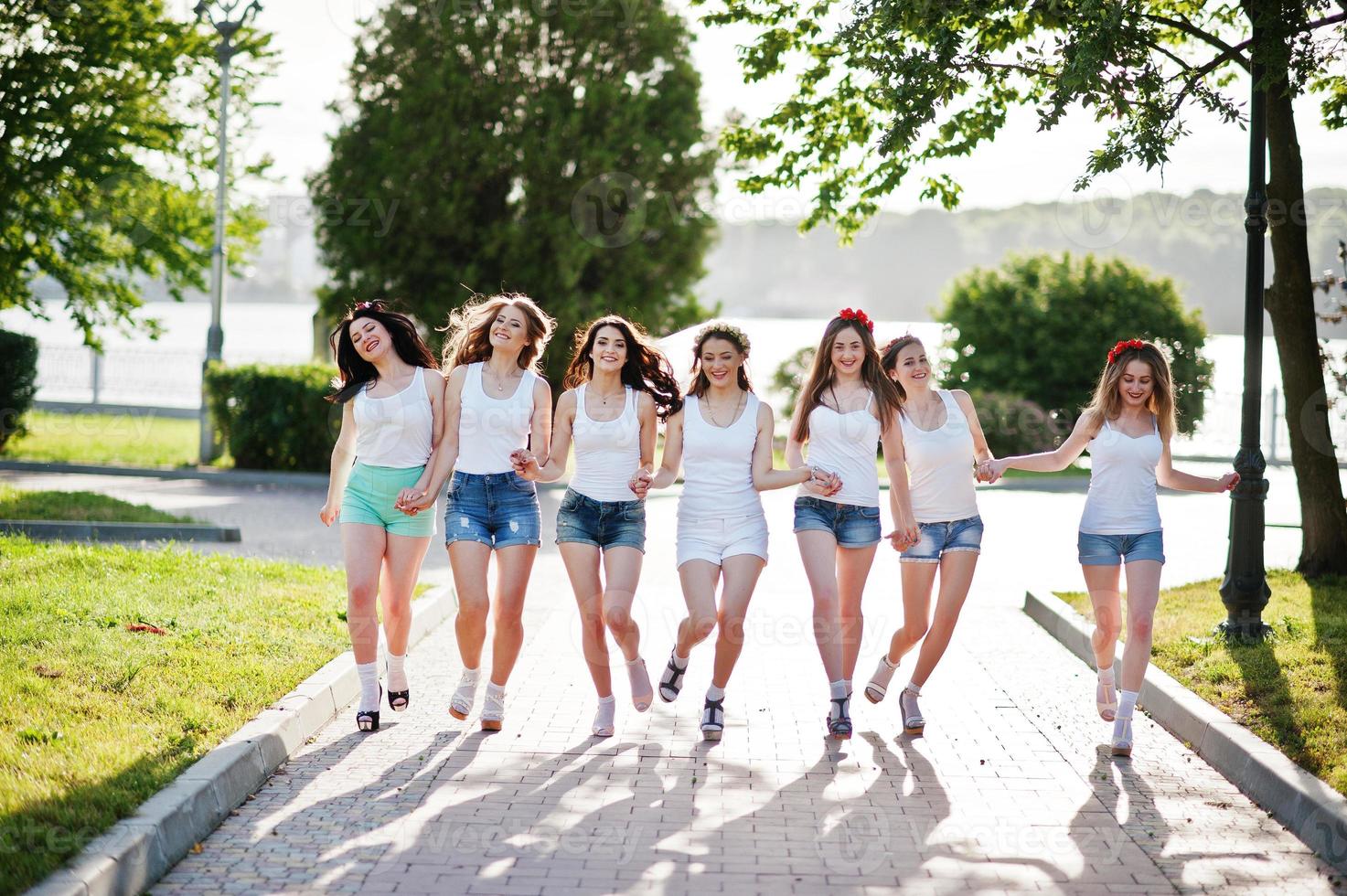 sete garotas felizes e sensuais em shorts curtos e camisas brancas se divertindo na estrada no parque na festa de despedida de solteira foto