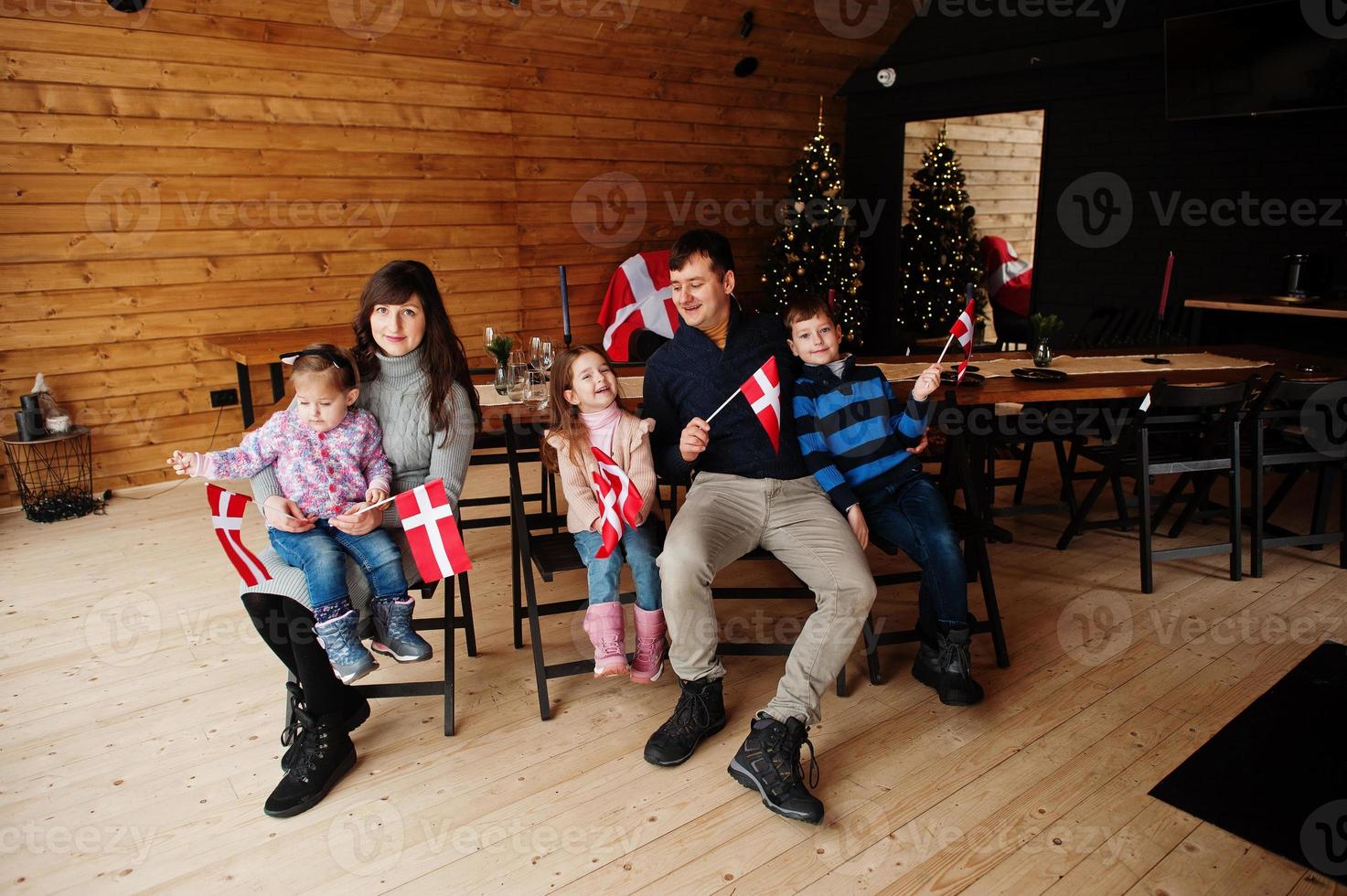 família com bandeiras da Dinamarca dentro de casa de madeira, sentado à mesa. viajar para países escandinavos. o povo dinamarquês mais feliz. foto