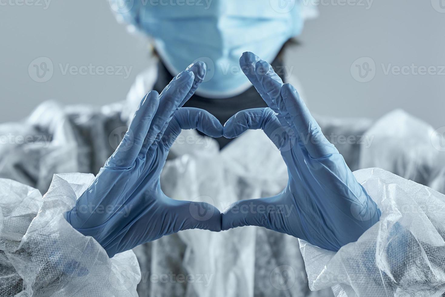 mulher com máscara médica em borrão e mãos na luva de látex mostra o símbolo do coração. foto