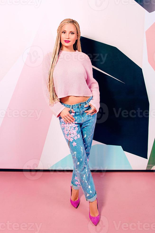 loira linda mulher sorridente com tranças africanas na camisola rosa e jeans em pé foto