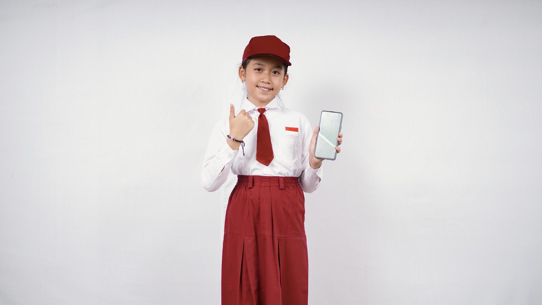 menina asiática do ensino fundamental mostrando a tela do smartphone e tudo bem isolado no fundo branco foto