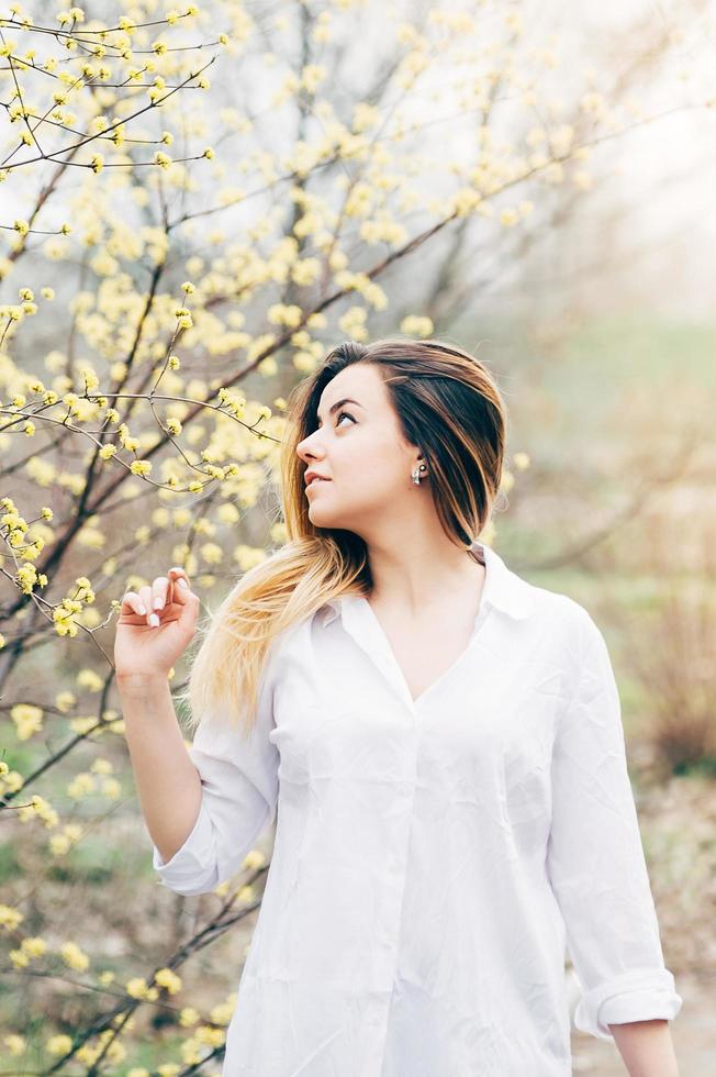 menina bonita no jardim gosta de florescer árvores com flores amarelas foto