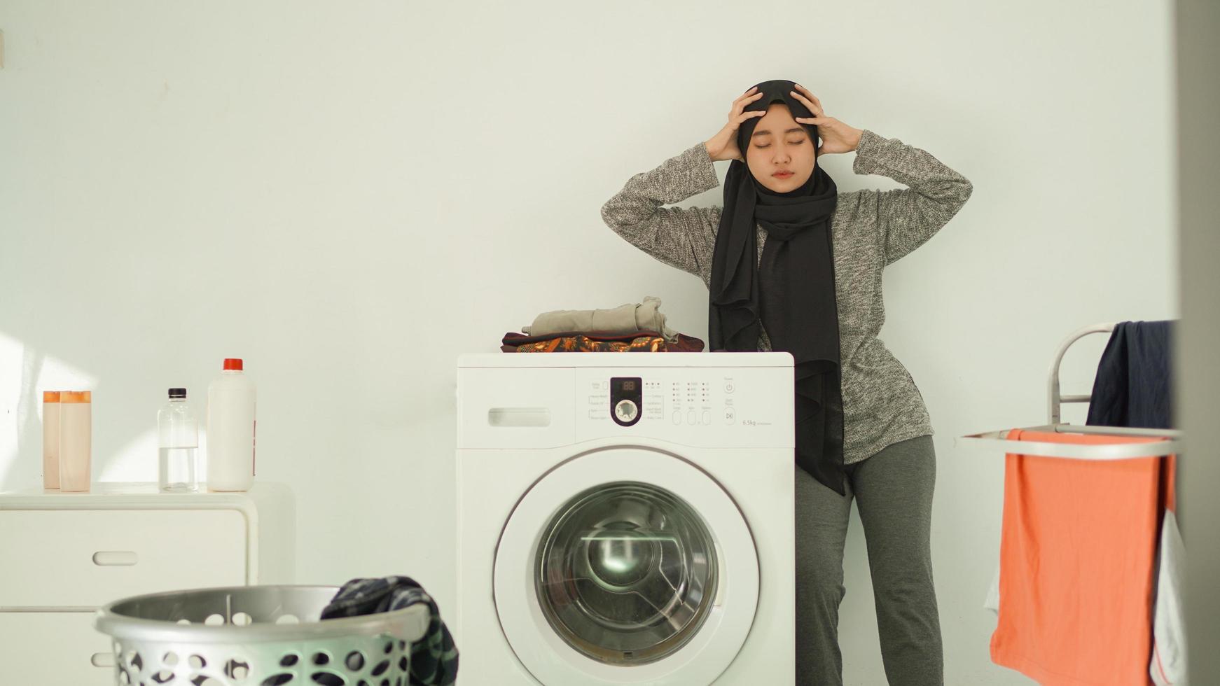 mulher asiática usando hijab estressa muita roupa em casa foto