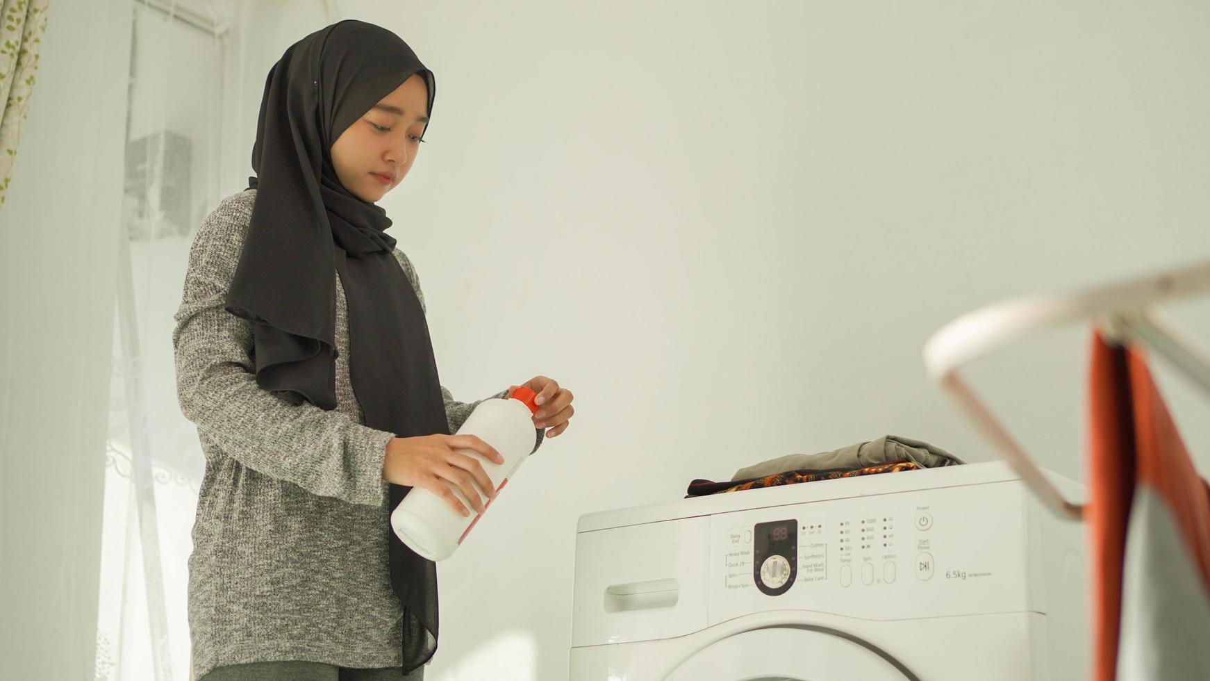 mulher bonita em hijab vai derramar detergente em sua roupa em casa foto