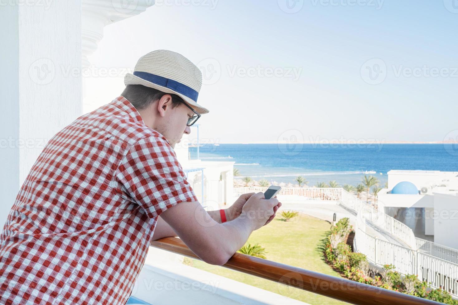 bonito jovem caucasiano em pé na varanda do hotel, usando telefone celular foto