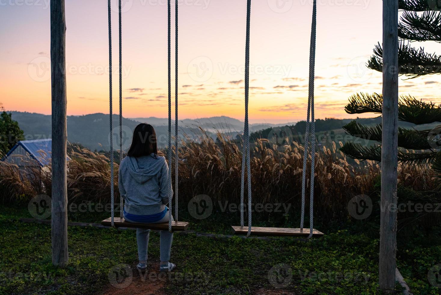 Vista lateral da mulher madura sentada na cadeira de balanço e olhando o nascer do sol durante as férias foto