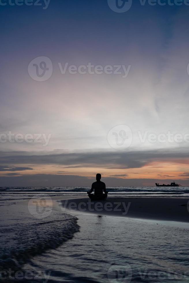 silhueta de homem meditar na praia ao pôr do sol foto