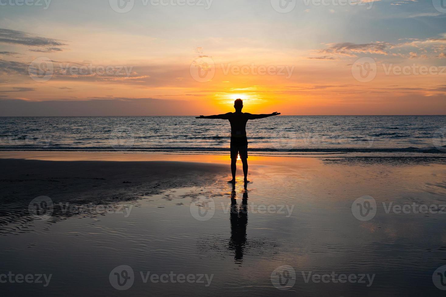 silhueta de homem stanidng na praia ao pôr do sol foto