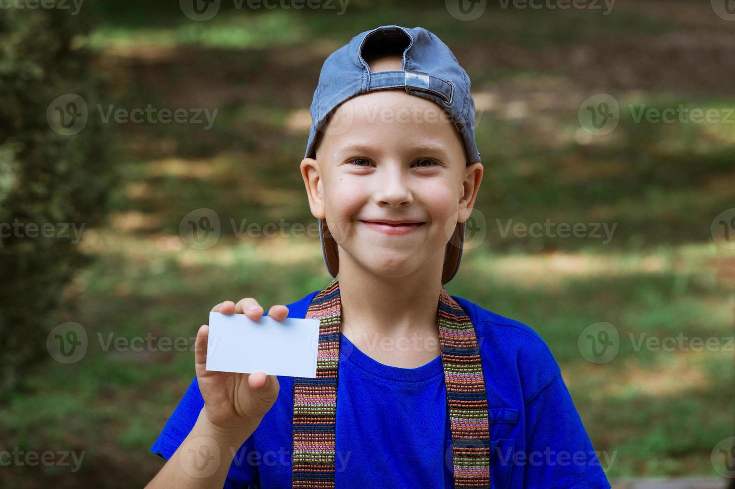 retrato de um menino de boné segurando um cartão de visita no parque foto