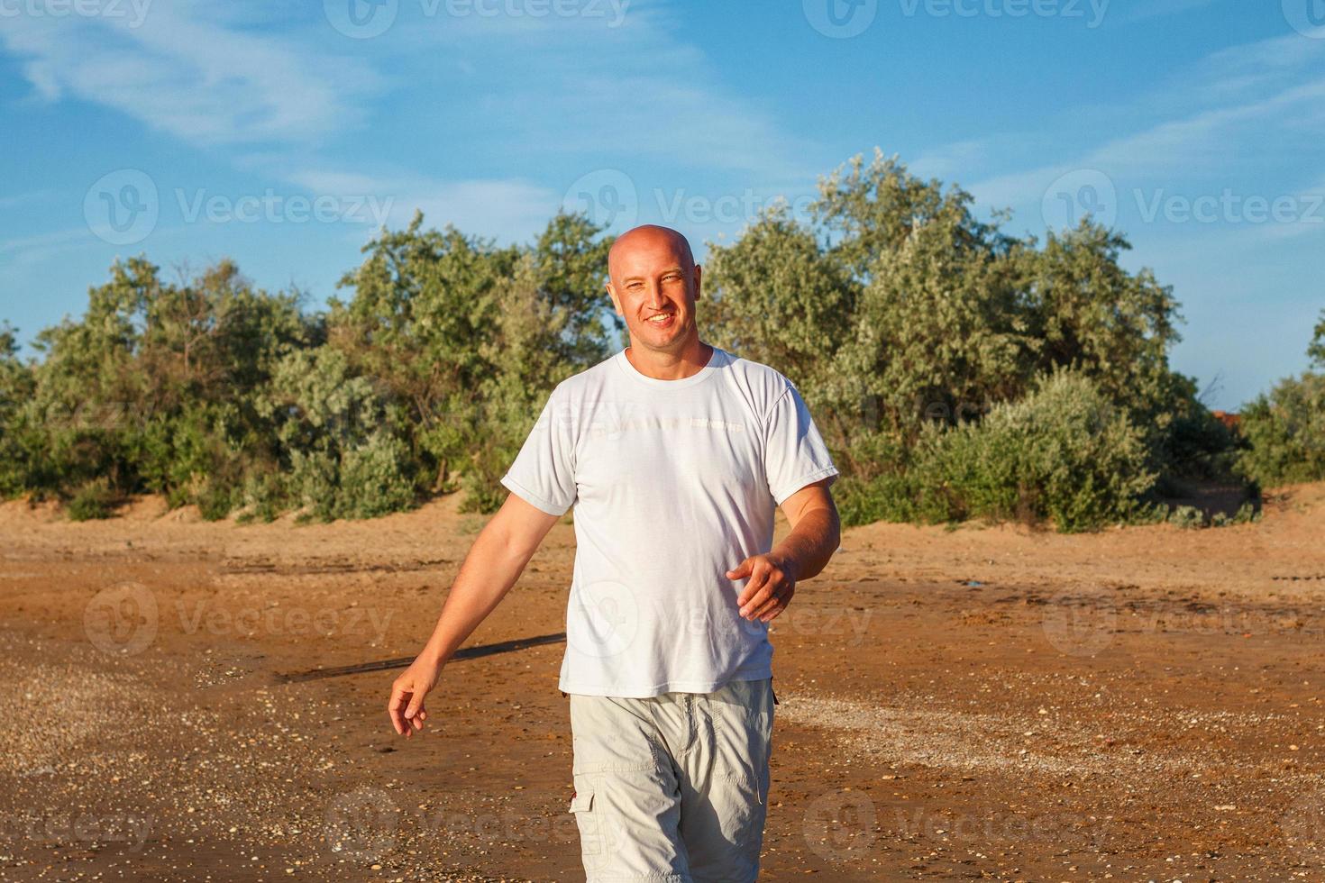 homem careca feliz andando na praia em roupas brancas foto