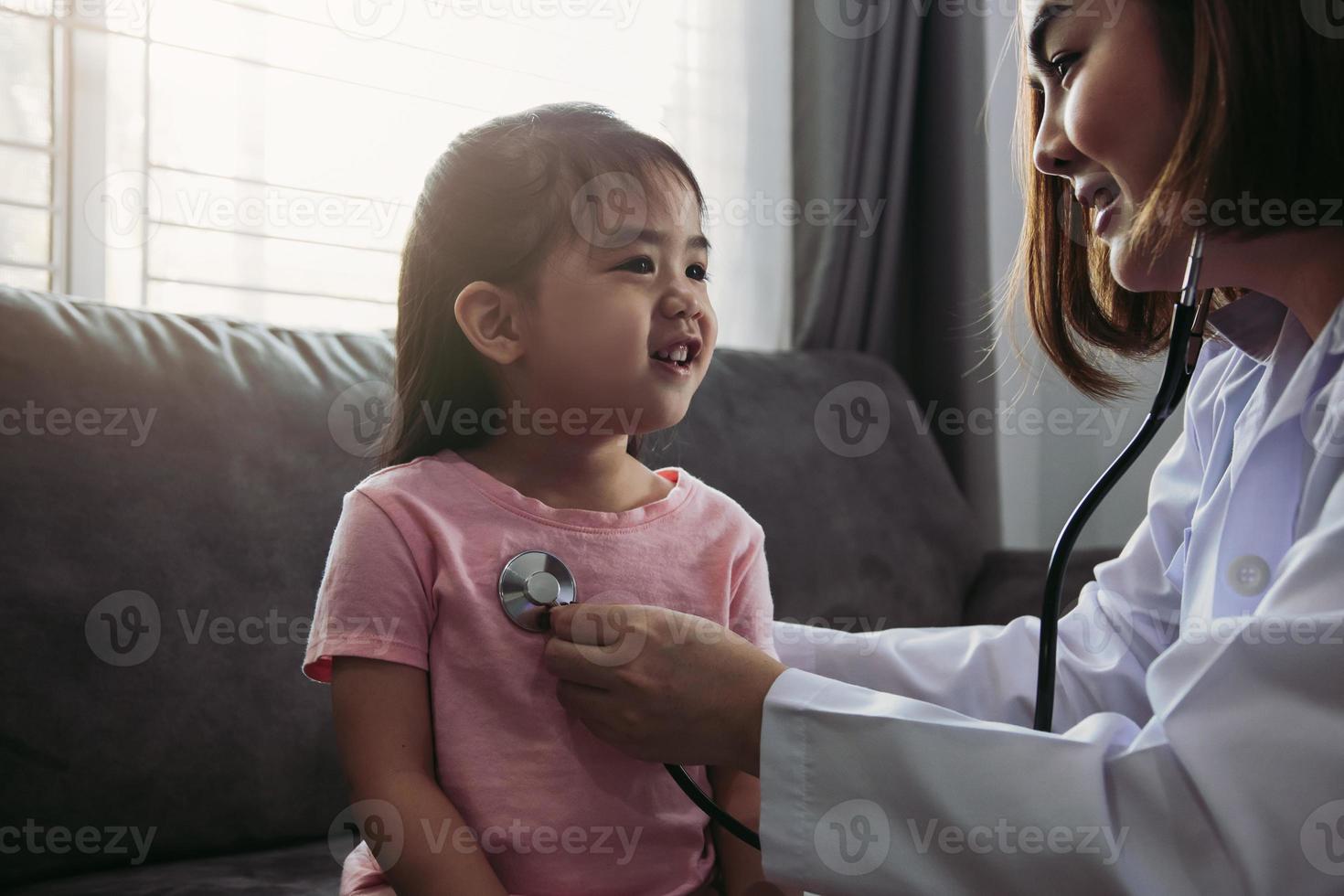 profissional de saúde de mulher asiática confiante visita seu paciente usando um estetoscópio durante uma jovem paciente do sexo feminino bem verificar em casa. foto