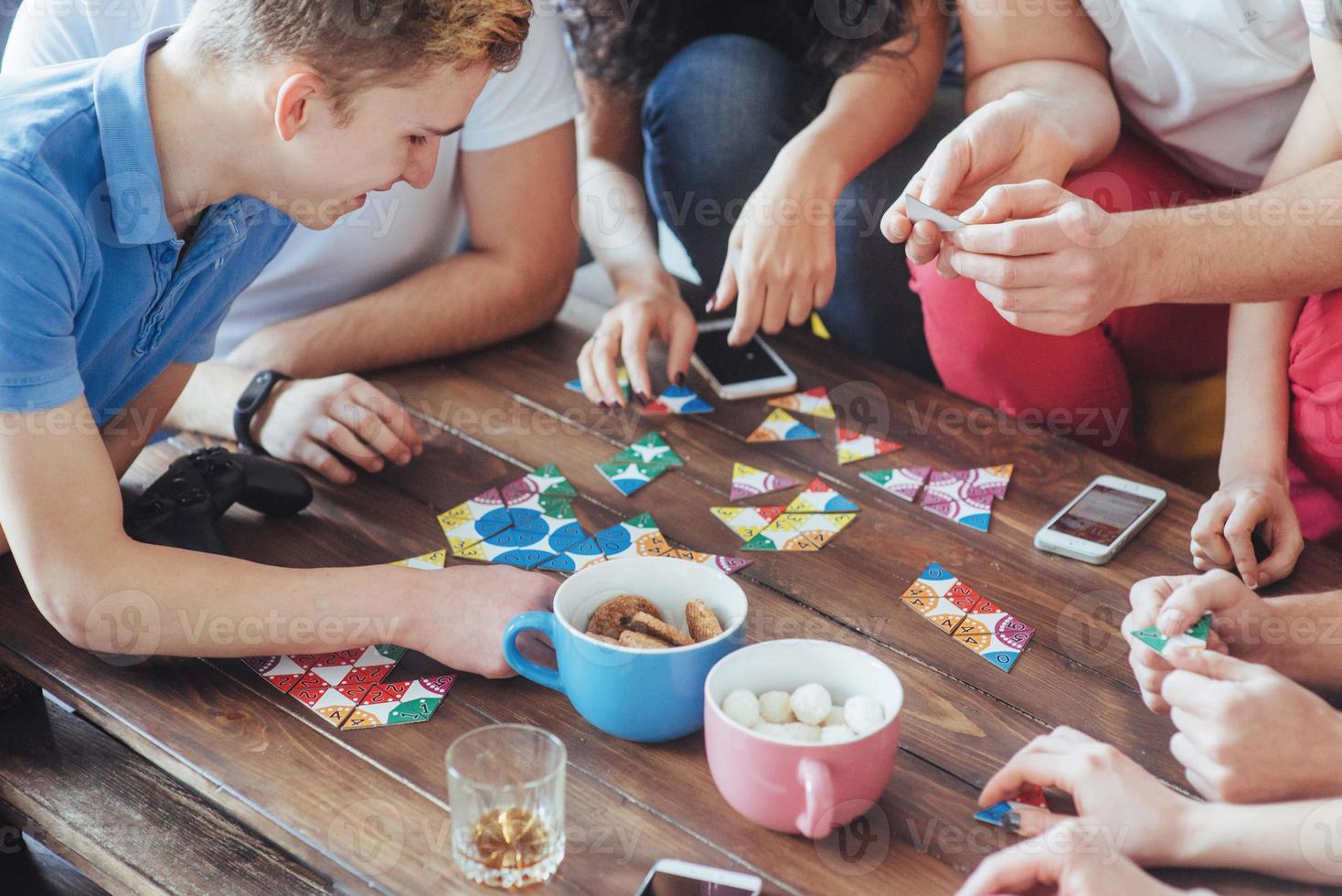 foto criativa de vista superior de amigos sentados à mesa de madeira. se divertindo jogando jogo de tabuleiro