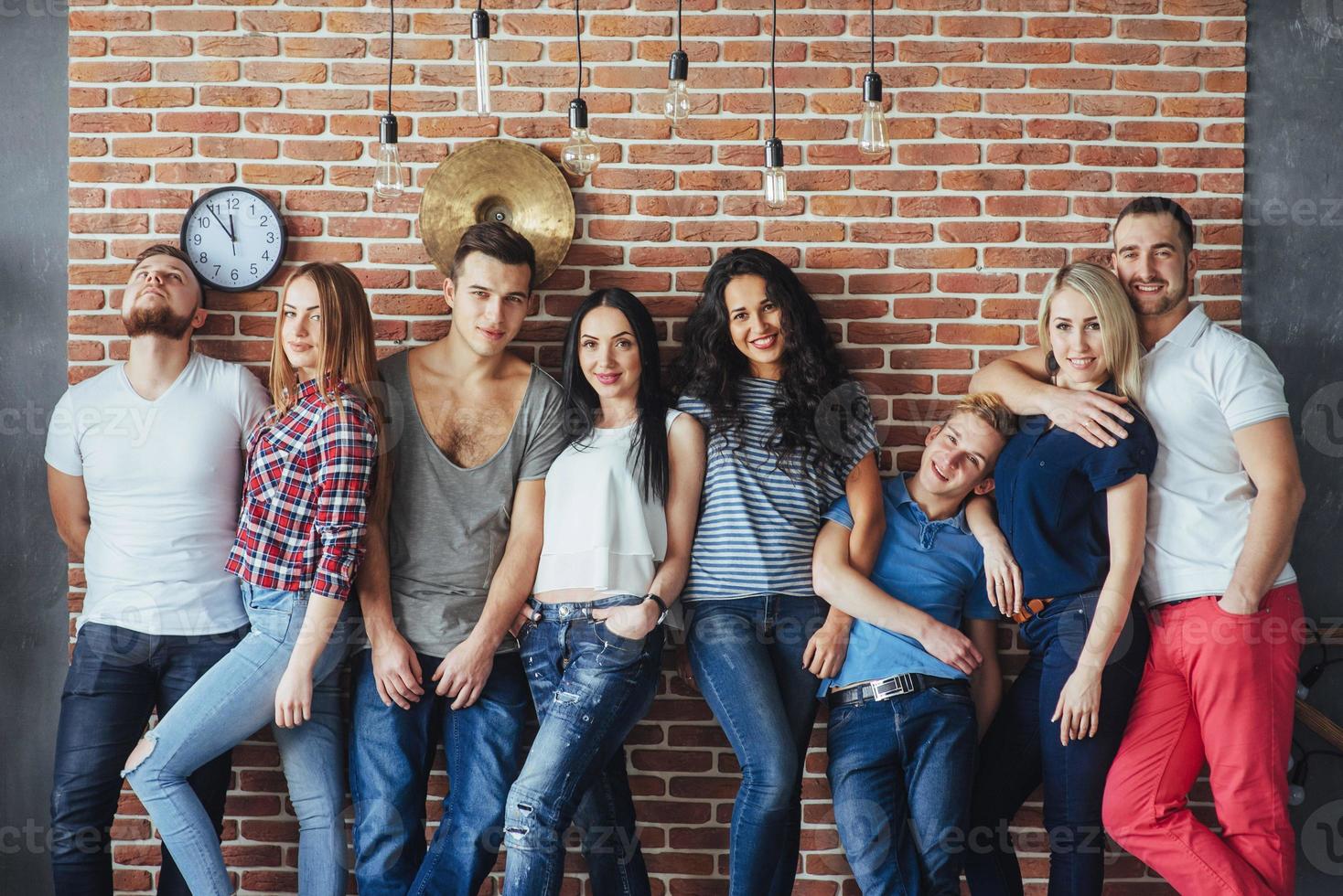 retrato de grupo de meninos e meninas multiétnicas com roupas coloridas da moda segurando amigo posando em uma parede de tijolos, pessoas de estilo urbano se divertindo, conceitos sobre estilo de vida de união juvenil foto