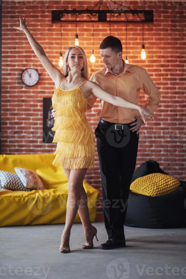 jovem casal dançando música latina. bachata, merengue, salsa. duas poses de elegância no café com paredes de tijolos foto