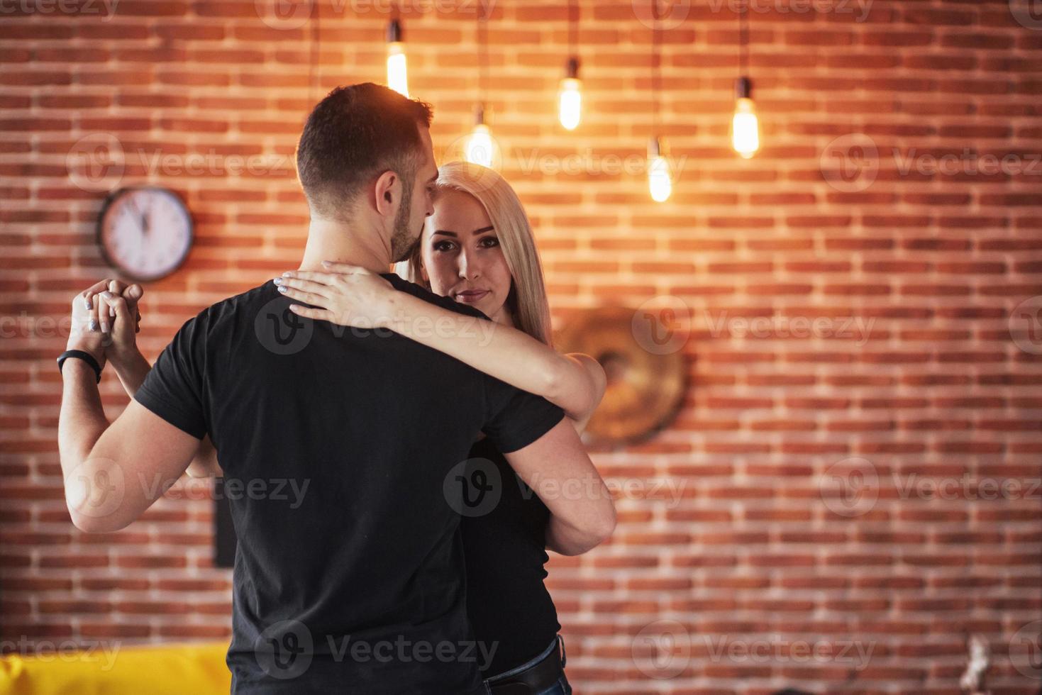 jovem casal dançando música latina. bachata, merengue, salsa. duas poses de elegância no café com paredes de tijolos foto