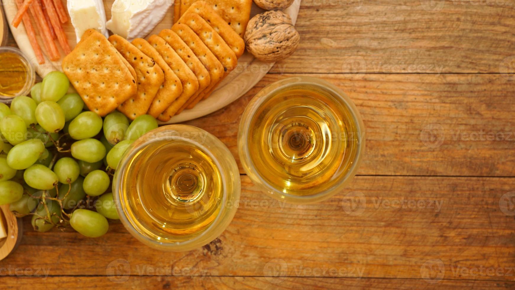 uvas verdes, bolachas, nozes e dois copos de vinho branco sobre fundo de madeira foto