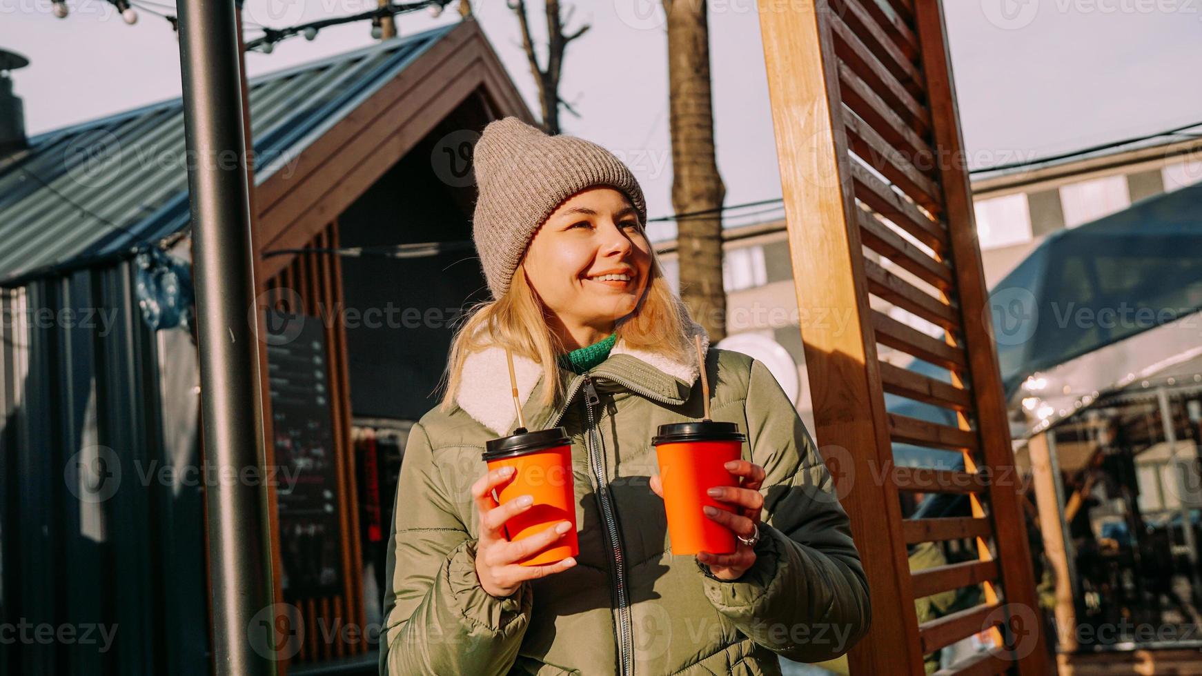 mulher carrega duas xícaras de café ou vinho quente na cidade fora da praça de alimentação foto