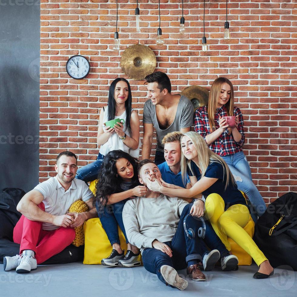 retrato de grupo de meninos e meninas multiétnicas com roupas coloridas da moda segurando amigo posando em uma parede de tijolos, pessoas de estilo urbano se divertindo, conceitos sobre estilo de vida de união juvenil foto