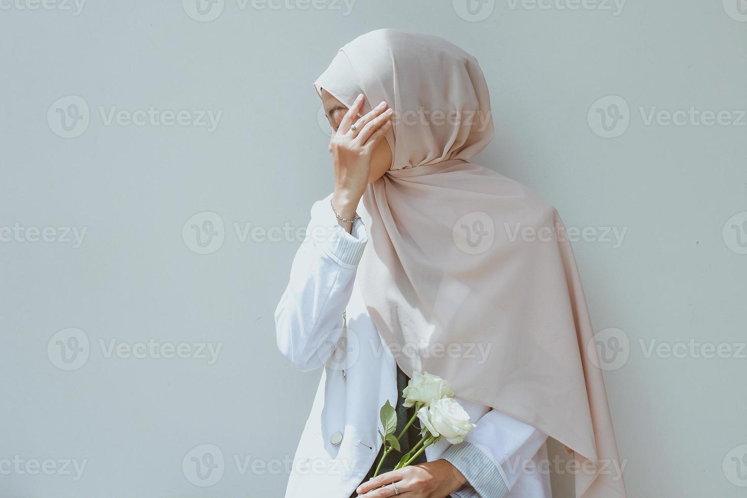 jovem muçulmana segurando rosa branca e cobrindo o rosto com a mão foto