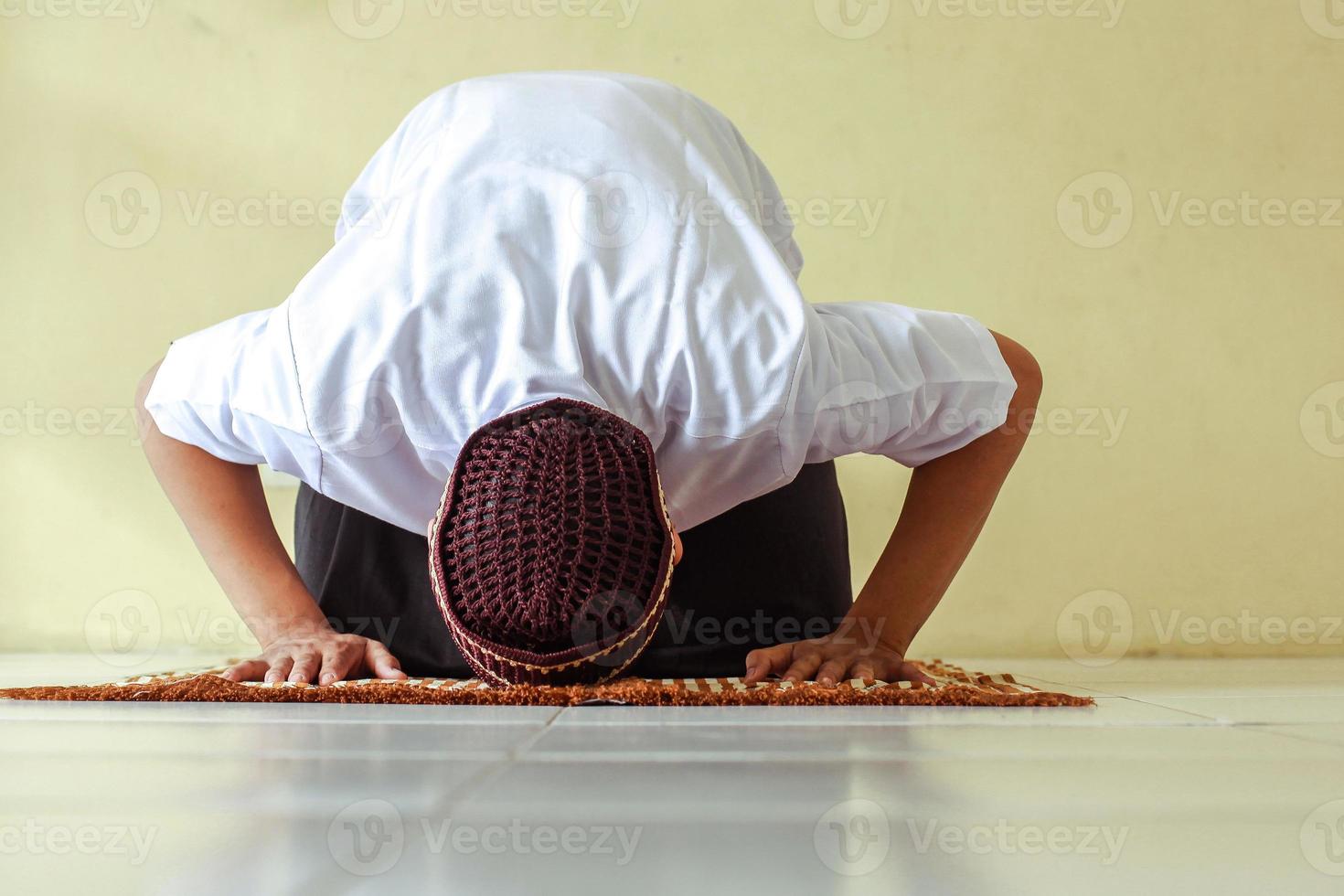 vista frontal do homem muçulmano fazendo salat com pose de prostração no tapete de oração foto