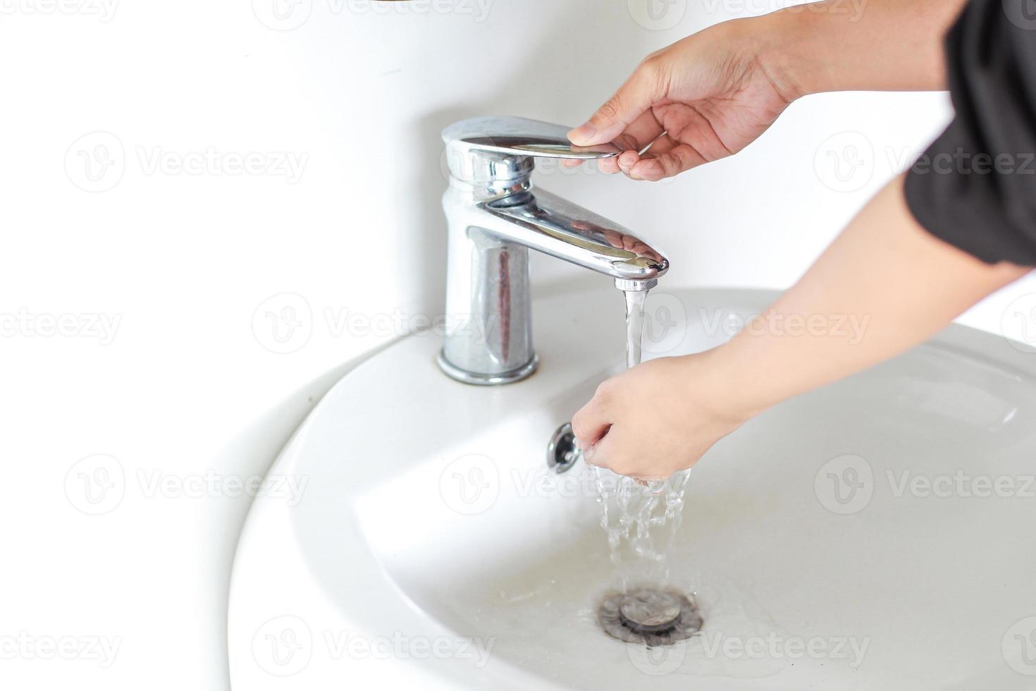 lavando as mãos na pia branca com água da torneira de metal foto