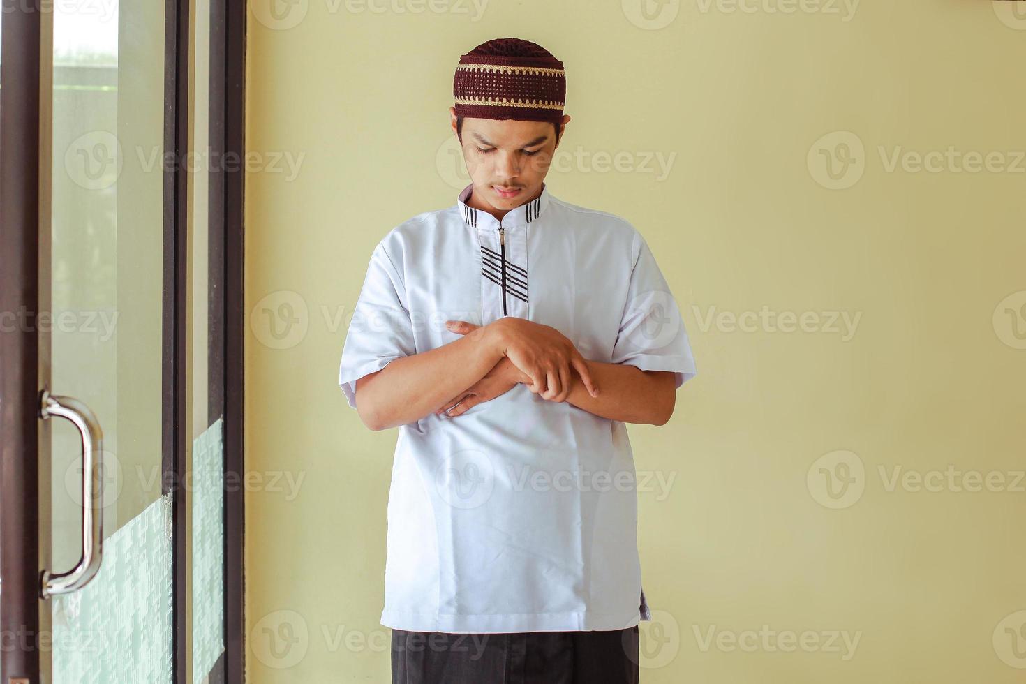 vista frontal do jovem muçulmano asiático fica com a mão no peito está fazendo salat na mesquita foto