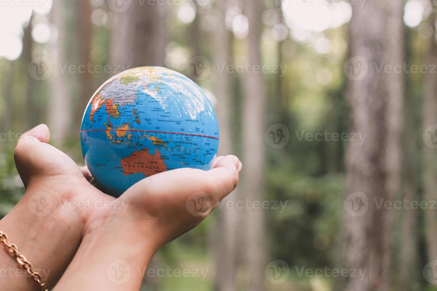 mão segurando o modelo de terra com árvores de floresta embaçada no fundo, conceito de dia da terra foto