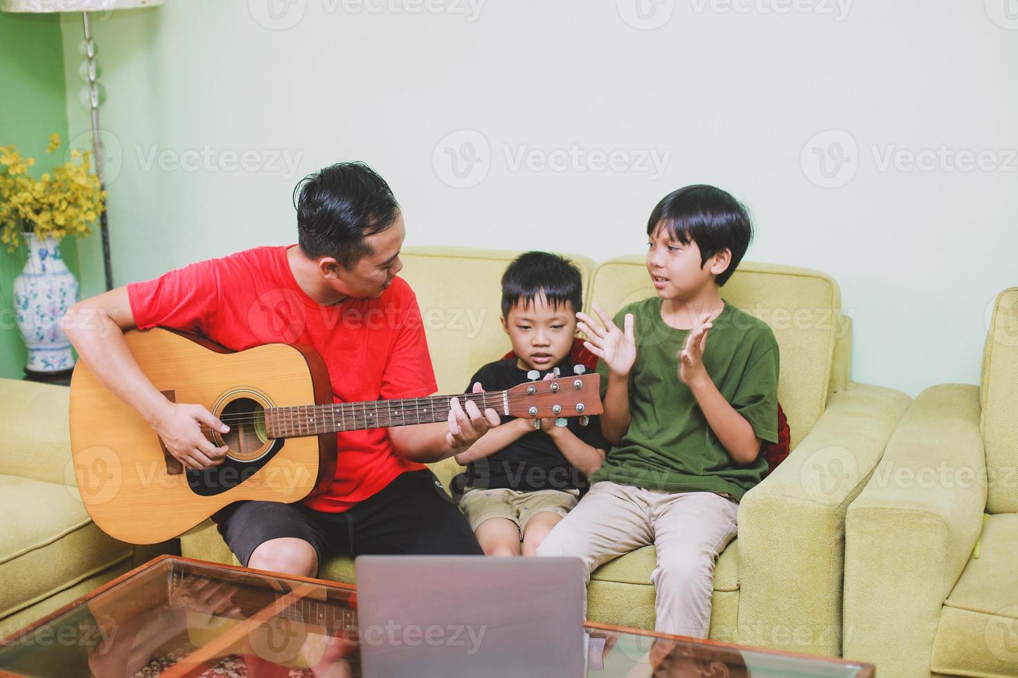 asiático pai e filho tocando violão e cantando junto com seu filho em casa foto