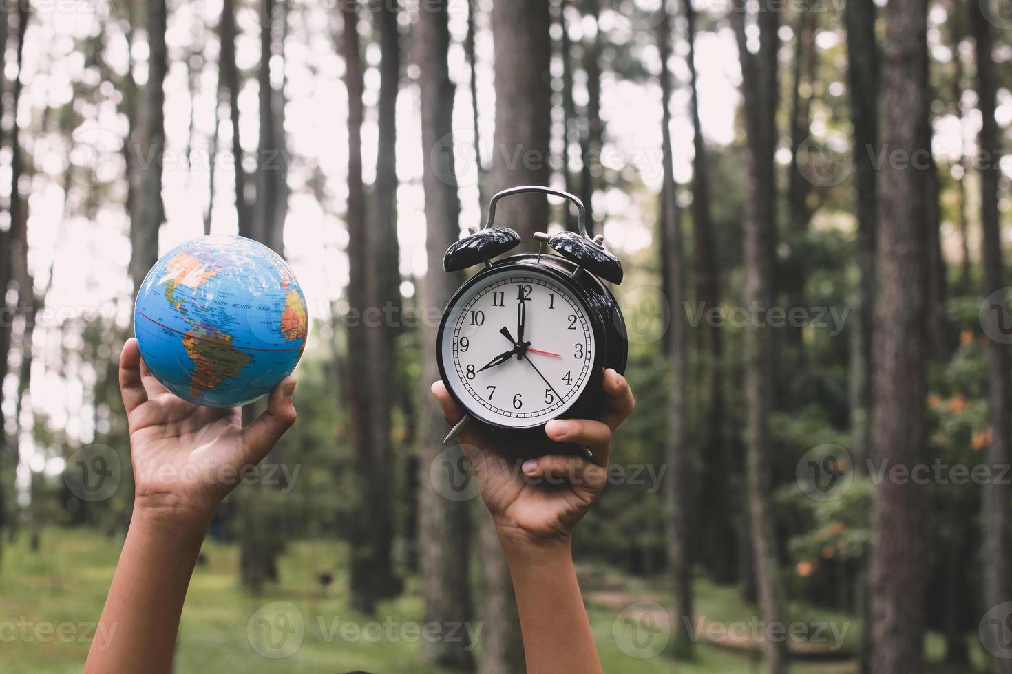 globo terrestre levantado à mão e despertador com embaçamento de árvores na floresta ao fundo, conceito de hora da terra foto