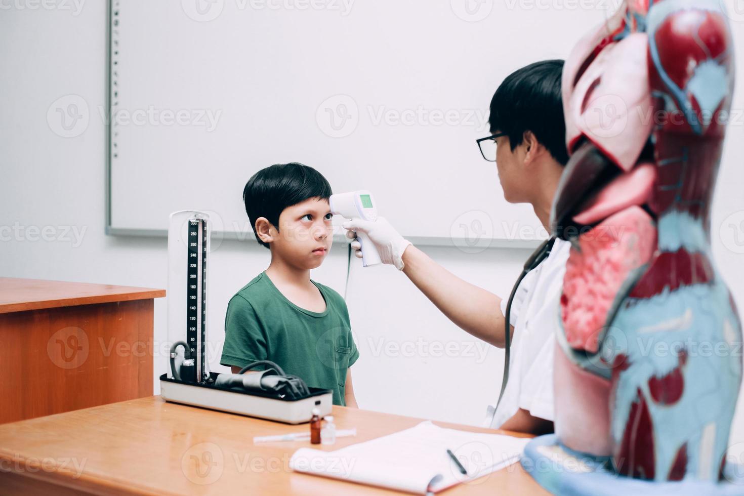 médico verificar a temperatura corporal do paciente menino usando arma termômetro infravermelho na testa foto