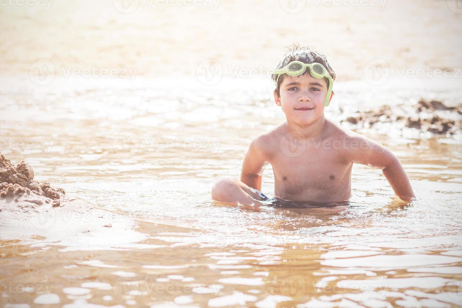 menino sorridente feliz sentado na praia foto