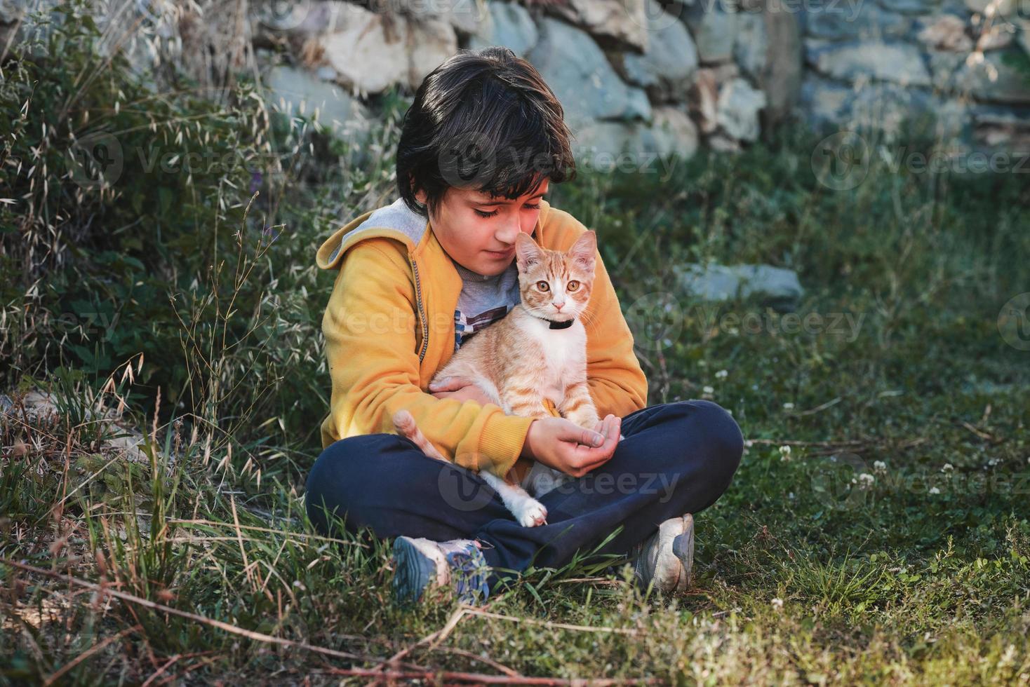 criança sentada na grama com seu gatinho foto