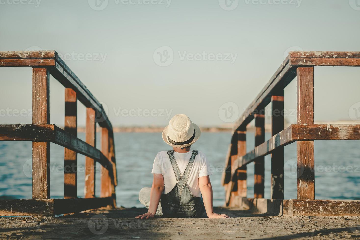 vista traseira de uma criança pensativa sentada olhando para o mar foto