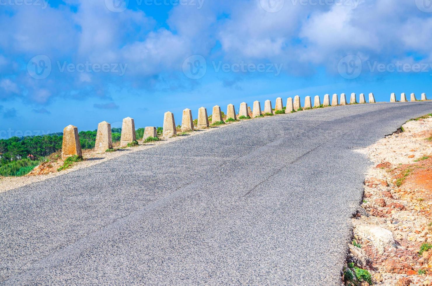 estrada de asfalto com cerca de barreira de guarda de pedra levando para a frente e para a direita, nuvens brancas de céu azul foto